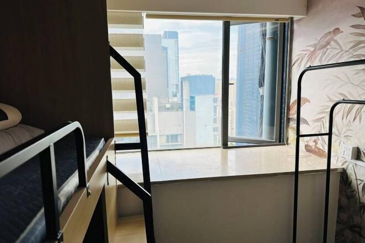 A room with a bunk bed, a desk, a window with a city view, and a patterned wall.
