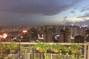 Ein nächtliches Stadtbild mit Hochhäusern und einem Balkon mit Pflanzen.