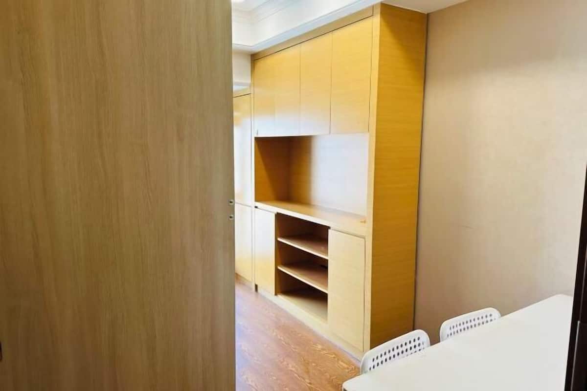 A room with a wooden cabinet, white chairs, and a wooden floor.
