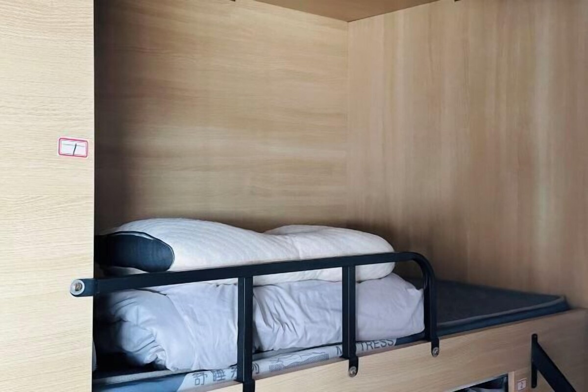 A bunk bed with a mattress and pillows, a wooden wall, and a small shelf.