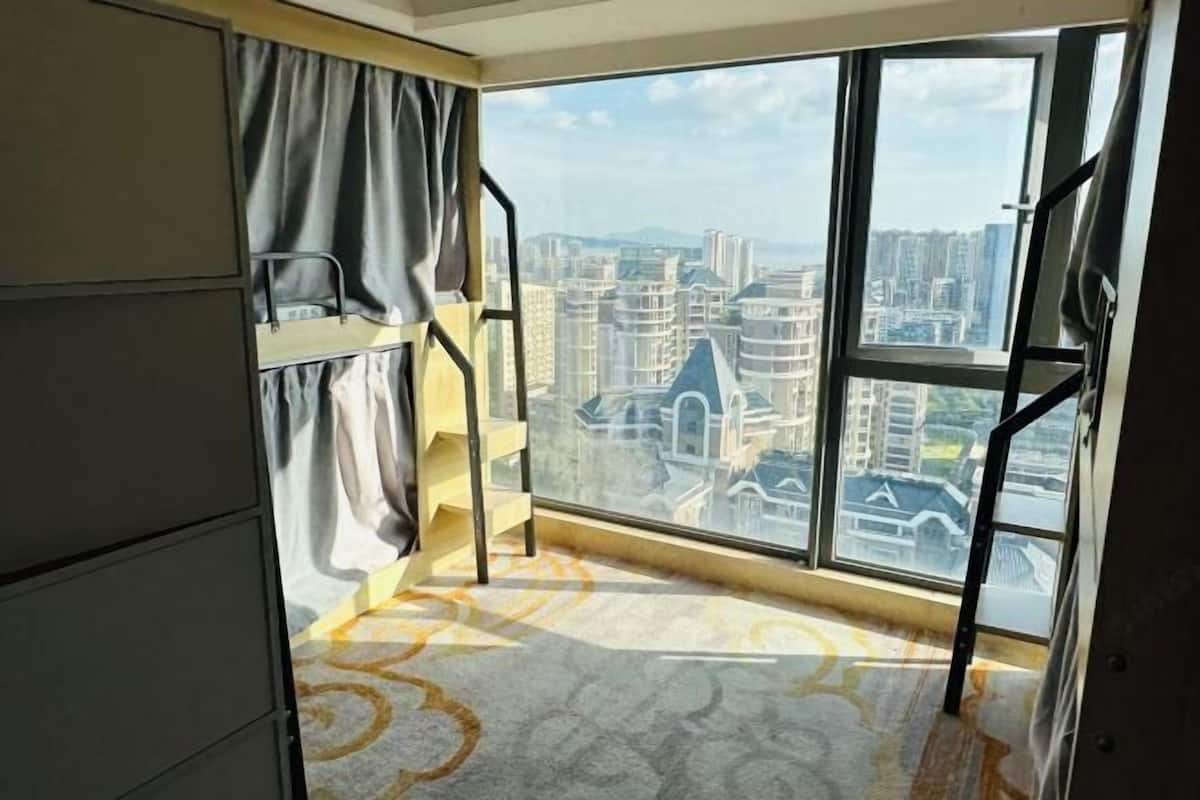 A room with a large window, a bunk bed, and a view of a cityscape.