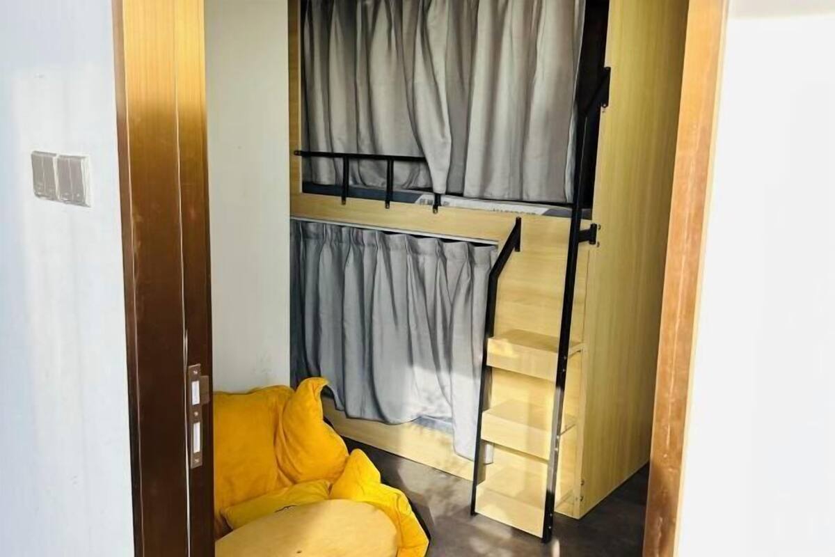 A room with a bunk bed, a yellow chair, and a curtain.
