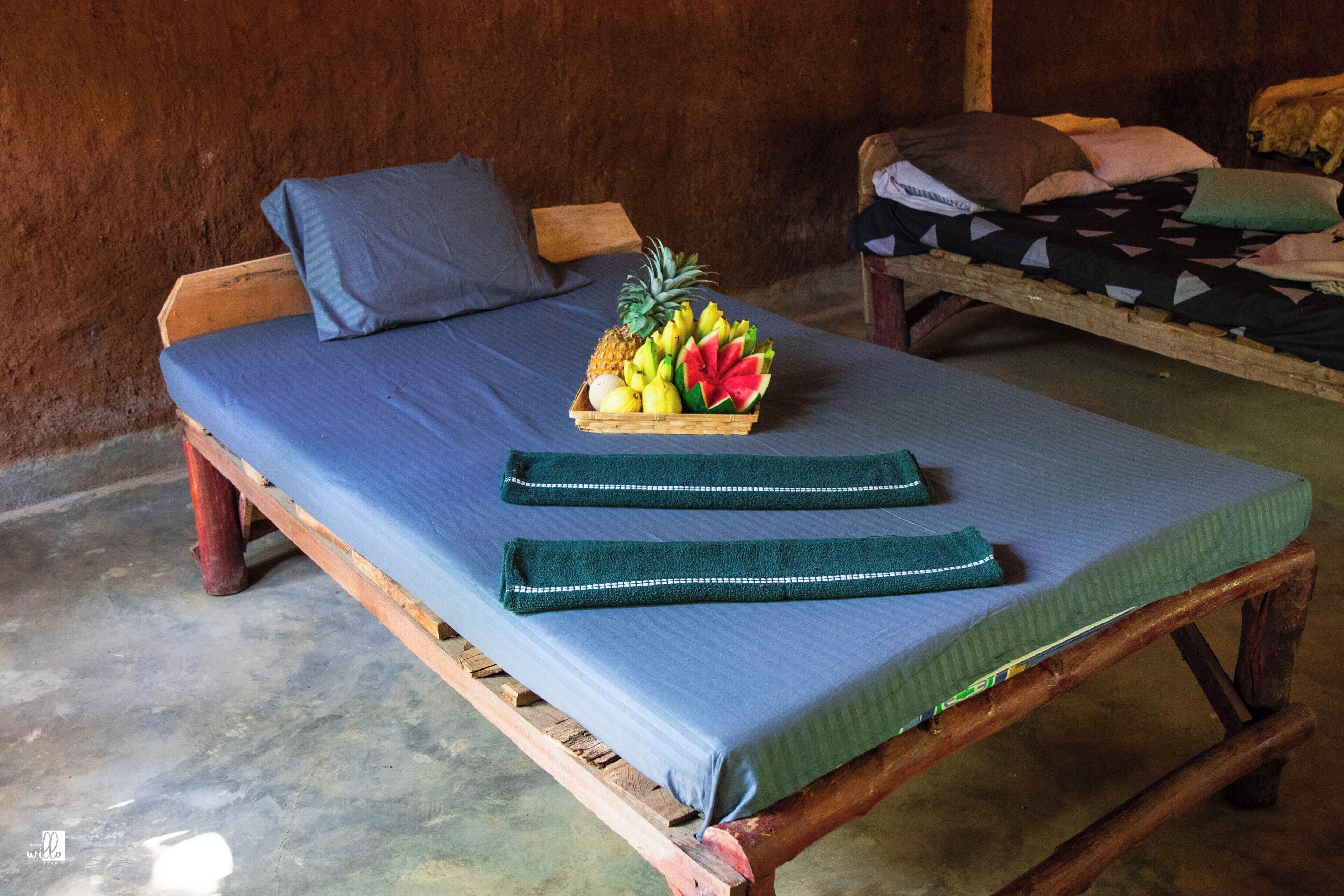 A simple wooden bed with a blue mattress and a fruit basket on it.