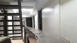 A corridor with a metal railing, a long table, and doors leading to rooms. - La Casa Parañaque (Paranaque)
