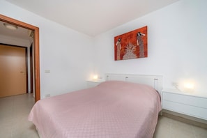 A bedroom with a bed, a nightstand, a wall-mounted painting, and a door.