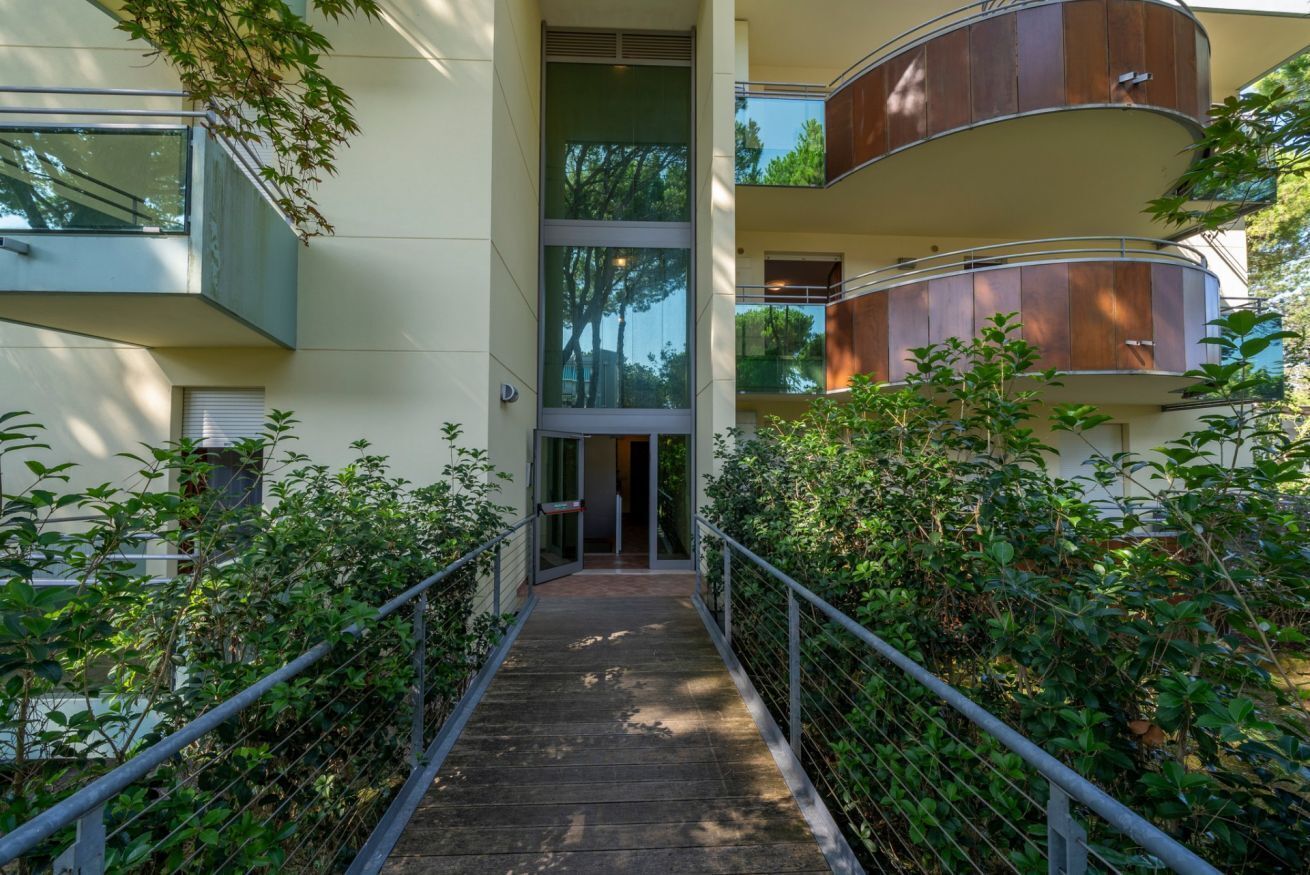 A modern building with a central glass entrance, a wooden walkway, and a metal railing.