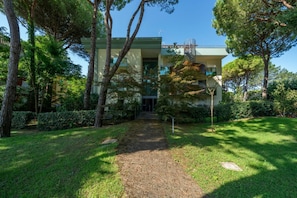 Um edifício com um caminho que leva à entrada, cercado por árvores e vegetação.