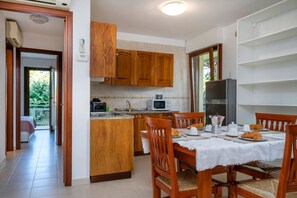 Une cuisine avec des meubles de rangement en bois, une table à manger entourée de chaises, un réfrigérateur et un four à micro-ondes.