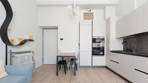 A modern kitchen with white cabinets, a dining table with chairs, a built-in oven, and a radiator.