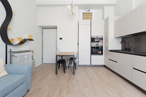 Una cocina moderna con armarios blancos, una mesa de comedor con sillas, un horno empotrado y un radiador.