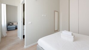 A bedroom with a bed, a wardrobe, a mirror, and a staircase leading to another room.