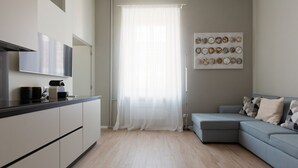 A modern kitchen with a flat-screen TV, a coffee machine, and a dining area with a light-colored sofa.