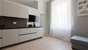 A modern kitchen with a flat-screen TV, a built-in oven, and a grey sofa.