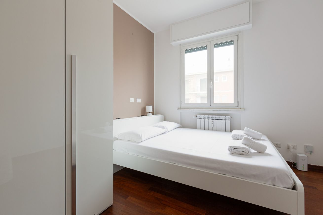 A single-bed room with a window, white walls, a radiator, and a wooden floor.