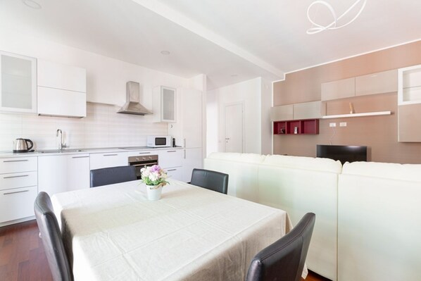 A modern kitchen with white cabinetry, a dining area with a table and chairs, and a white sofa.