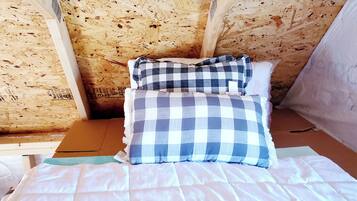 A room with a wooden ceiling, a bed with a white and blue checkered bedspread, and a pillow with a similar pattern.