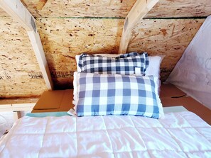 Une pièce avec un plafond en bois, un lit recouvert d’une couette à carreaux blancs et bleus, et un oreiller orné d’un motif similaire.