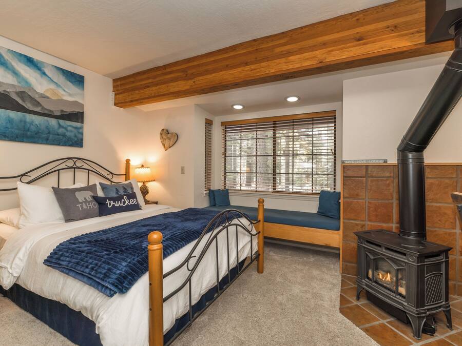 A bedroom with a bed, a bench, a fireplace, and a window with blinds.