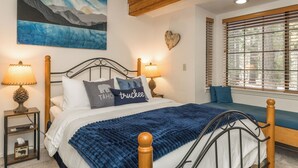 A bedroom with a bed, bedside lamps, a painting, a heart-shaped decoration, and a window with blinds. - Donner Lake Inn (Truckee)