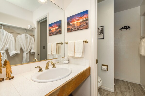 Une salle de bain avec un lavabo blanc, des robinets dorés et un miroir. Il y a deux tableaux au mur, un porte-serviettes et des toilettes.