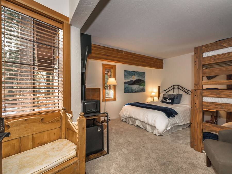 Une chambre confortable avec un lit superposé, un banc en bois, un bureau avec un ordinateur et un tableau accroché au mur.