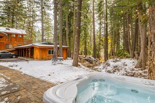 A wooden cabin with a hot tub in a snowy forest.