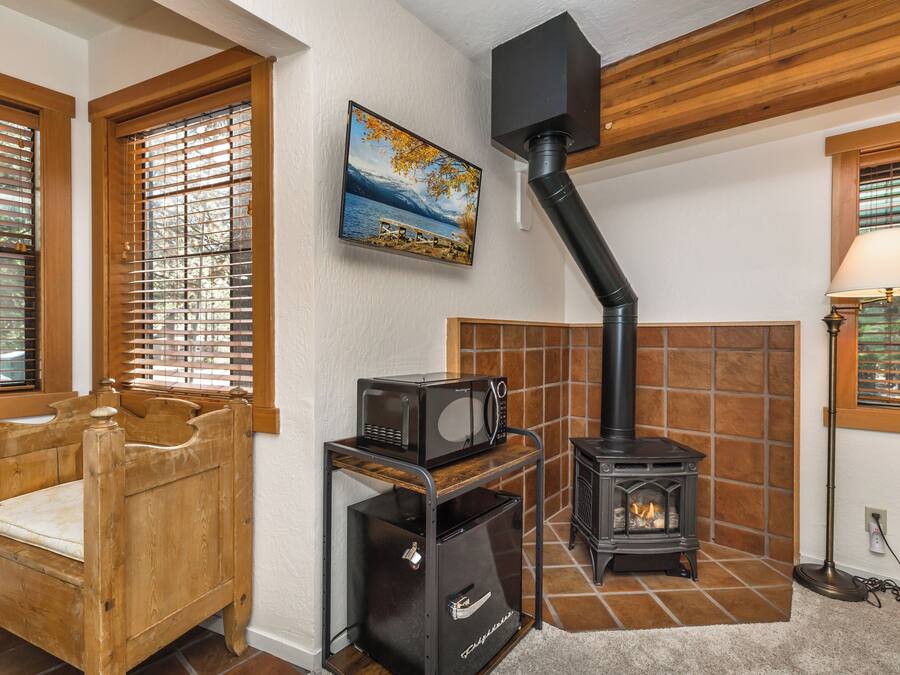 A cozy room with a wooden bed, a small black heater, a fireplace, and a painting of a lake.