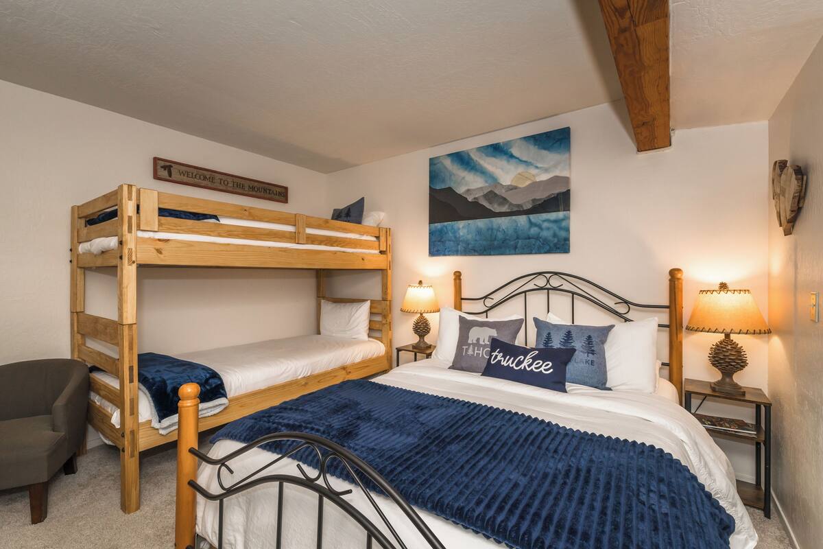 Une chambre avec un lit superposé, une pancarte de bienvenue, un tableau représentant une montagne, deux lampes de chevet et un coussin orné d'un motif de camion.