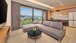 Ein modernes Wohnzimmer mit einem Ecksofa, einem schwarzen Couchtisch mit einer Vase, einem Flachbildfernseher und einem großen Fenster mit Blick auf die Stadt.