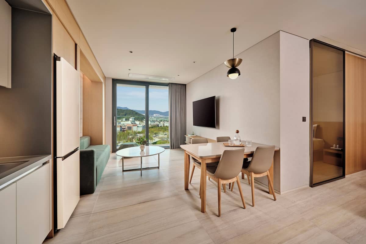 A modern living room with a dining area, a flat-screen TV, and a view of a cityscape through large windows.