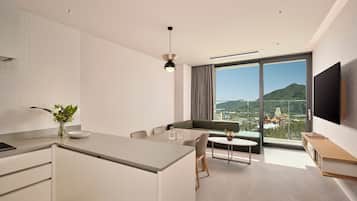 A modern hotel room with a kitchen, dining area, and a large window offering a city view.