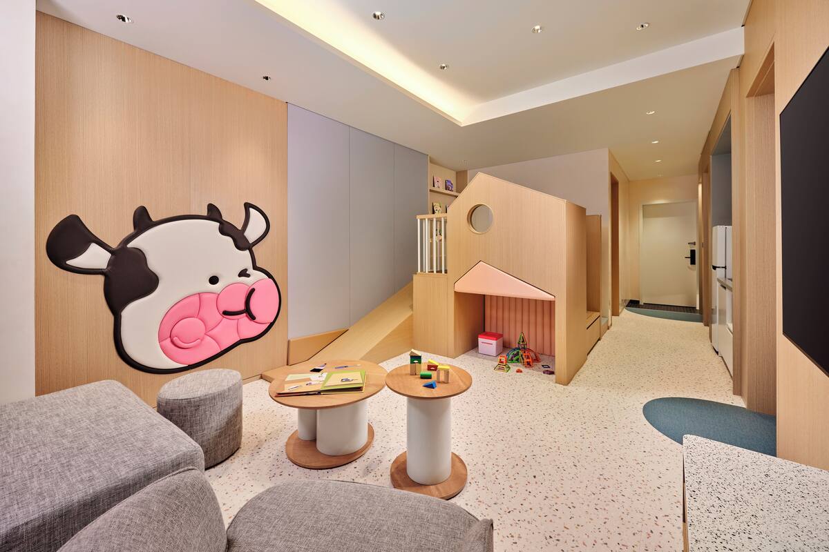 A children's play area with a large wall mural, two round tables, and grey cushioned seating.
