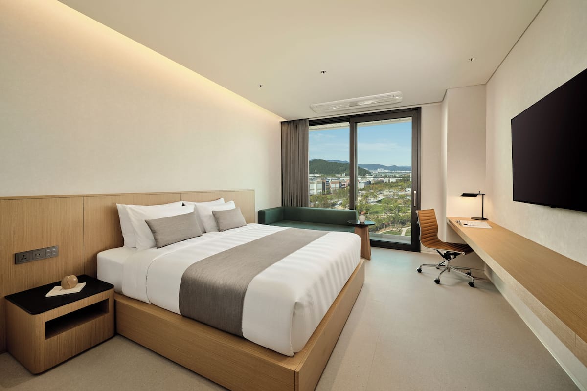 A modern hotel room with a large bed, a desk, a chair, and a TV.