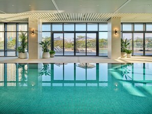A modern indoor swimming pool with clear glass walls, potted plants, and a view of the cityscape. - Lotte Hotel & Resort Gimhae (Gimhae)