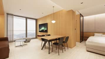 A modern hotel room with a large bed, a dining area with a table and chairs, a TV mounted on the wall, and a view of the city through large windows.