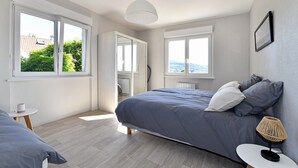 Ein modernes Schlafzimmer mit Bett, Nachttischen, einer Lampe und großen Fenstern.
