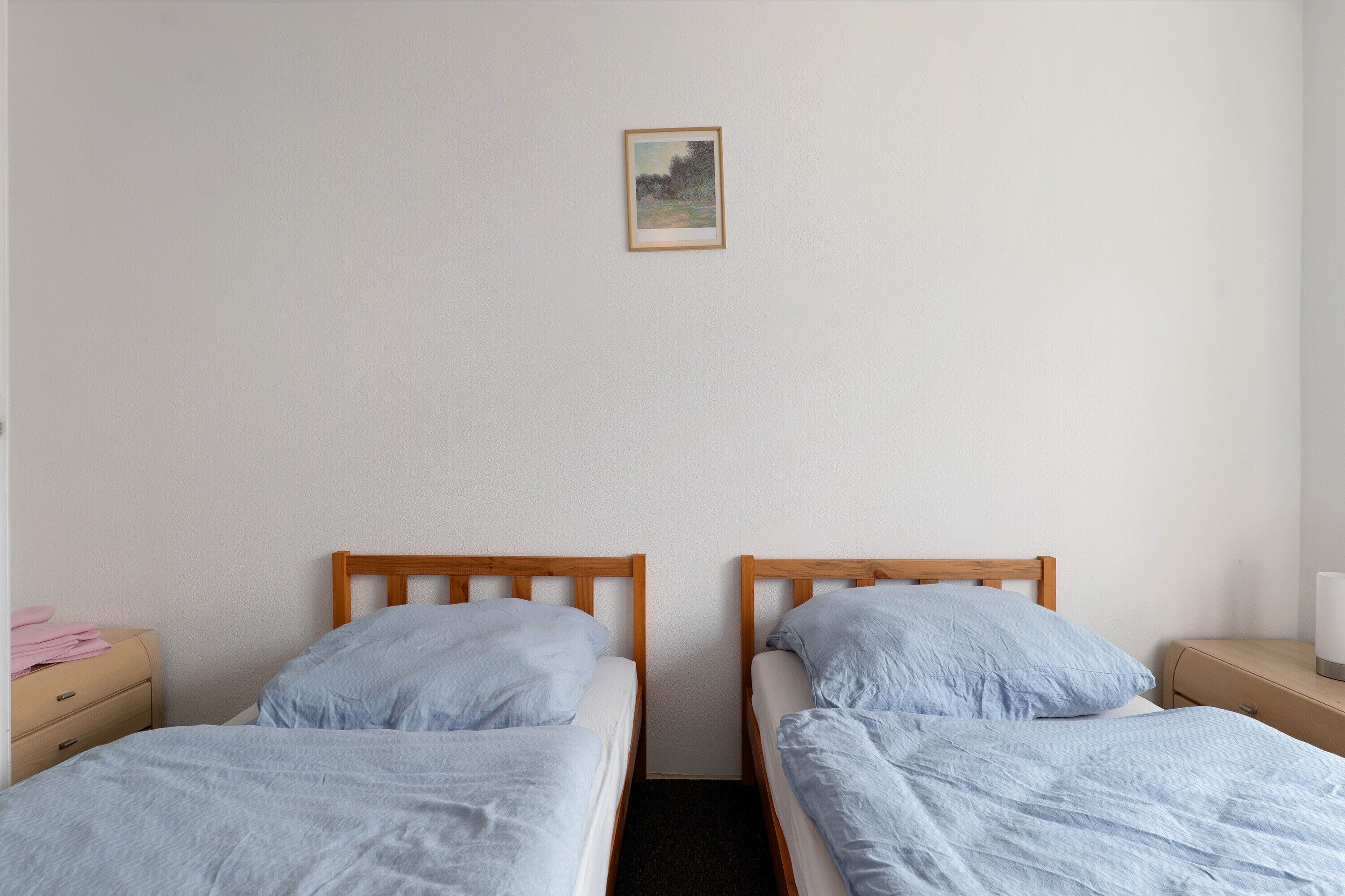 A twin room with two single beds, a small bedside table, a nightstand, and a framed picture on the wall.
