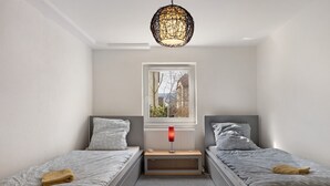 Un dormitorio con dos camas, una ventana, un radiador y una lámpara colgante.