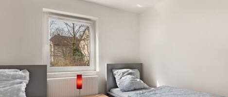 A bedroom with a window, a bedside table, a lamp, and a bed.