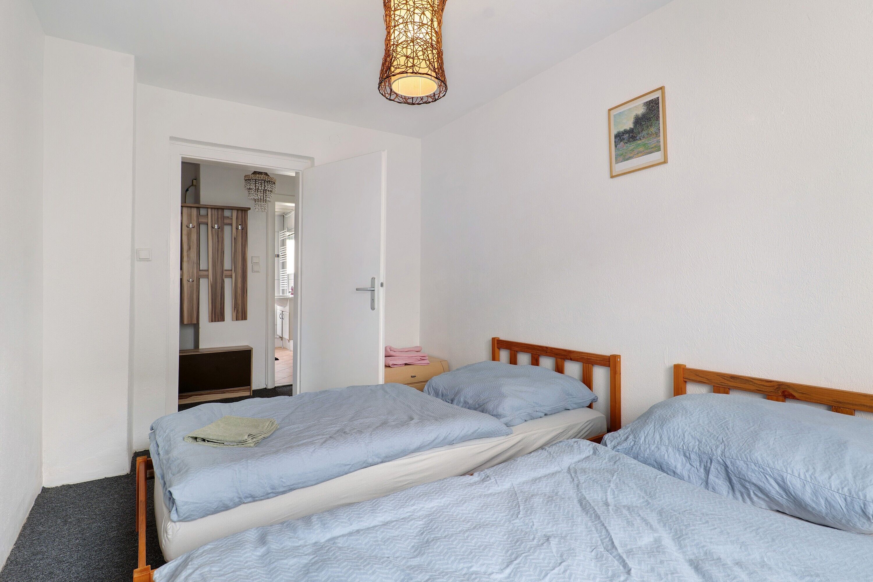 A bedroom with two beds, a wooden headboard, a bedside table with a lamp, and a door leading to another room.