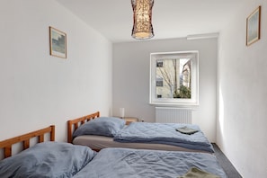 Quarto com duas camas, janela com vista, radiador e luminária pendente.