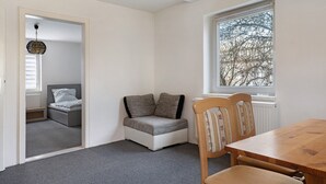 Una habitación con una cama, un pequeño rincón de descanso, una mesa de madera y una ventana con vistas a árboles.