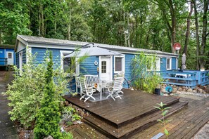 A blue cabin with a deck, white chairs, and a table.