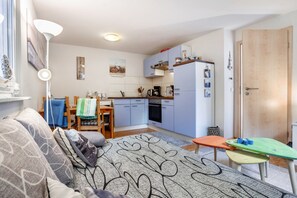 A compact living space with a kitchenette, a sofa, a dining table, and a small green table.
