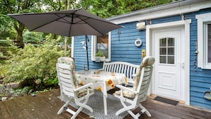 Une maison bleue avec une porte blanche, une véranda avec une table et des chaises, et un grand parasol.