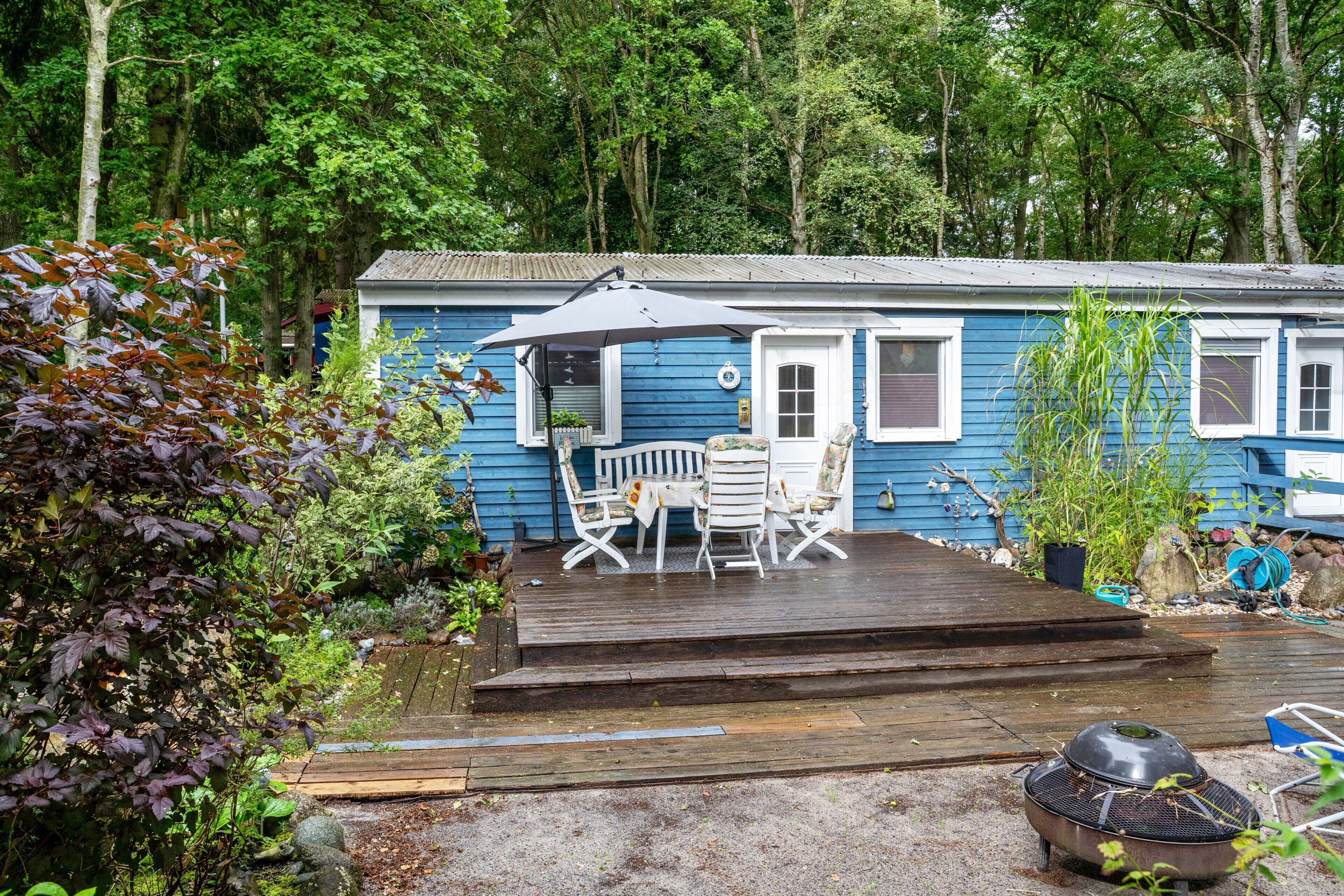 Une maison bleue avec une terrasse en bois, du mobilier d’extérieur et un jardin.