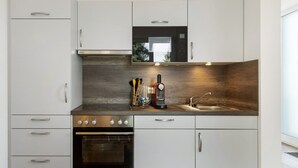 A modern kitchen with white cabinetry, a built-in oven, a microwave, and a sink.