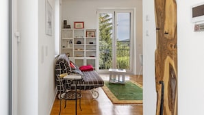 A modern living room with a sofa, a small table, a bookshelf, and a view through a glass door.