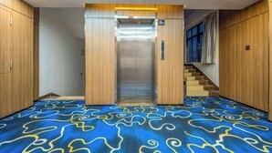 Un ascensor moderno con pantalla digital, alfombra de diseño azul, paredes de madera y una escalera con cortina azul.