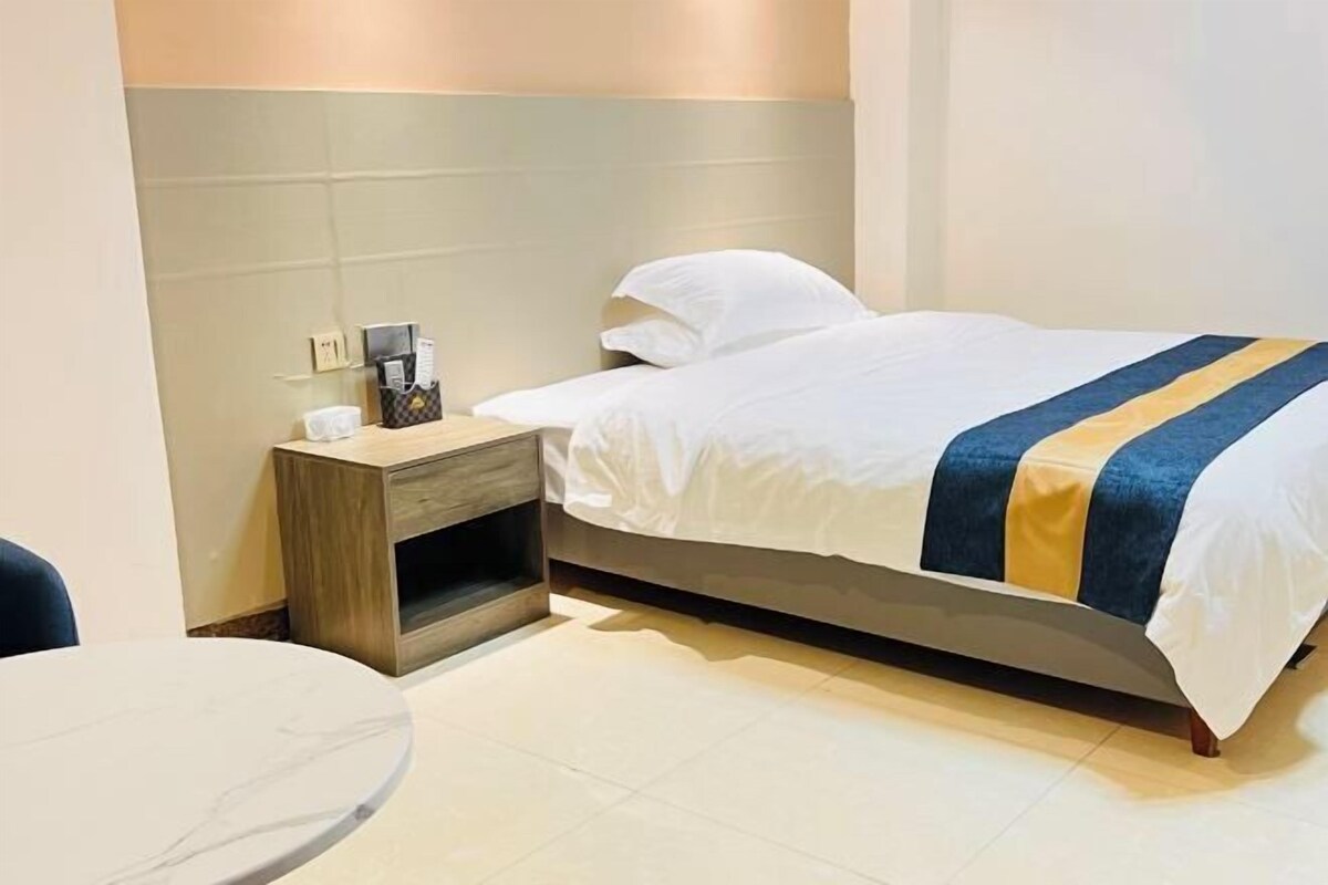 A hotel room with a bed, a bedside table, a chair, and a small round table.